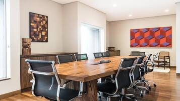 Uma sala de conferências com mesa de madeira, cadeiras pretas e duas pinturas abstratas nas paredes.