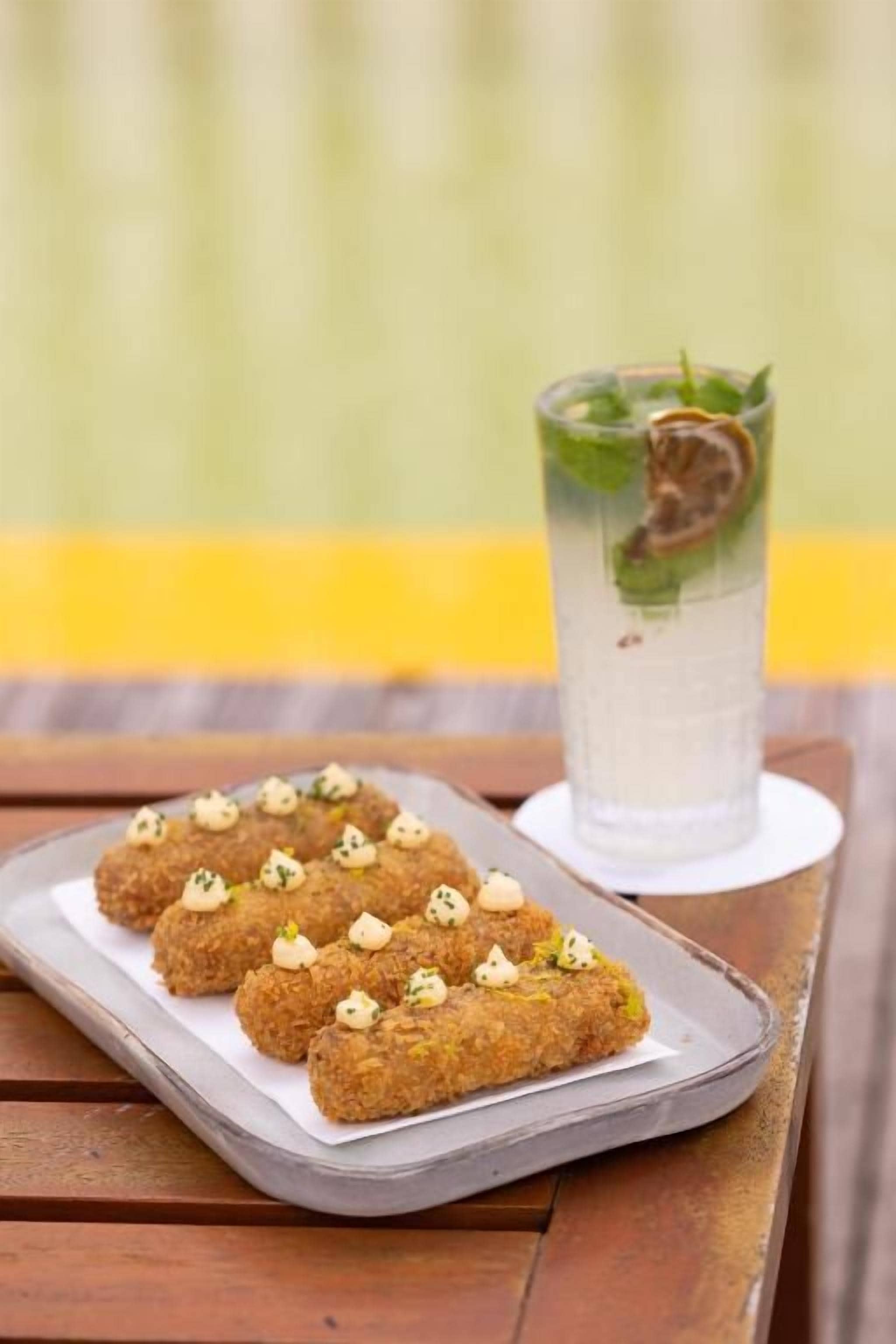 Un plateau contenant divers aliments et un verre d’une boisson claire, agrémentée d’une garniture, posés sur une table en bois.
