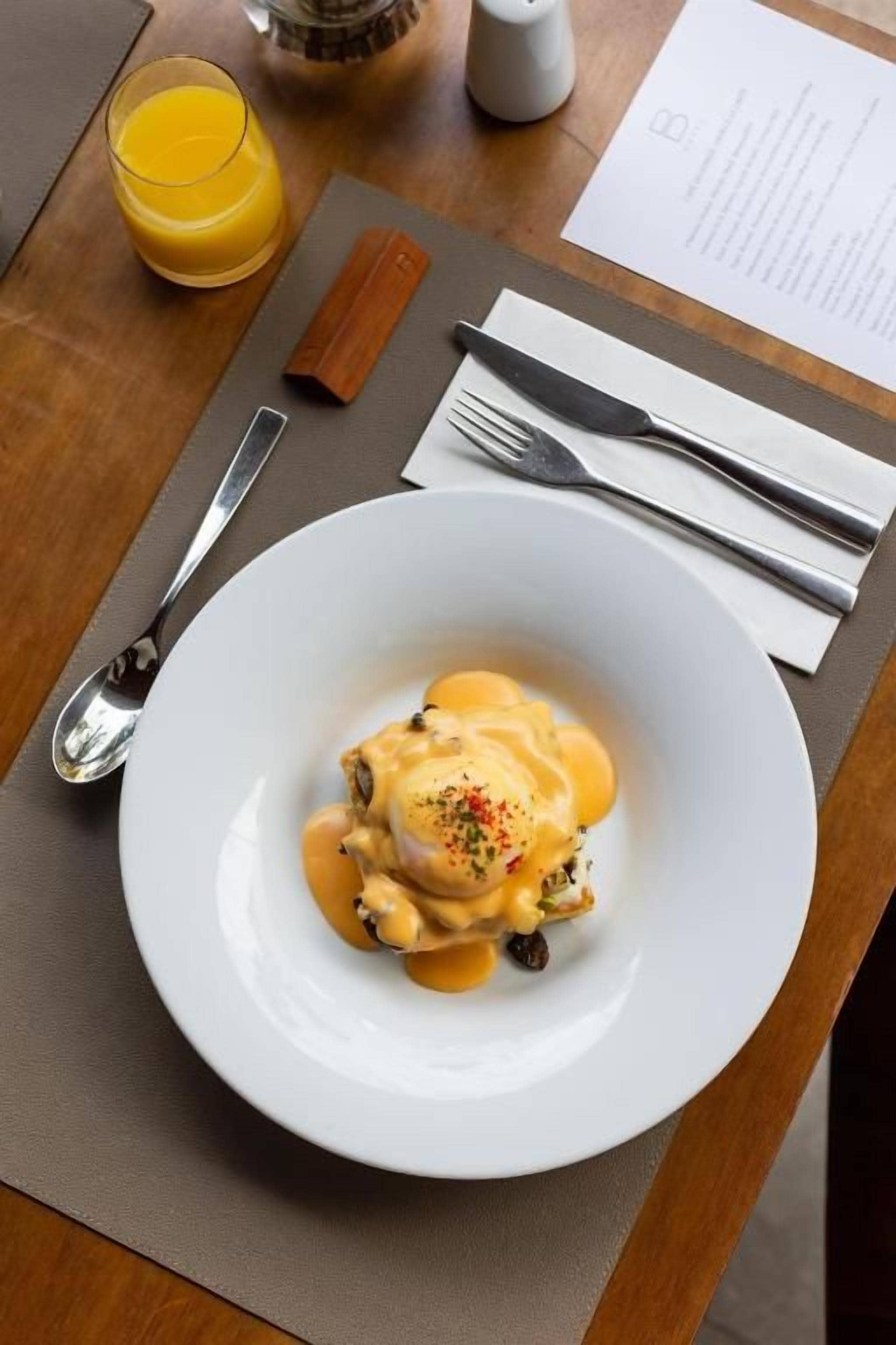 Un plato blanco con una porción de comida, un vaso de jugo de naranja y un menú sobre una mesa de madera.