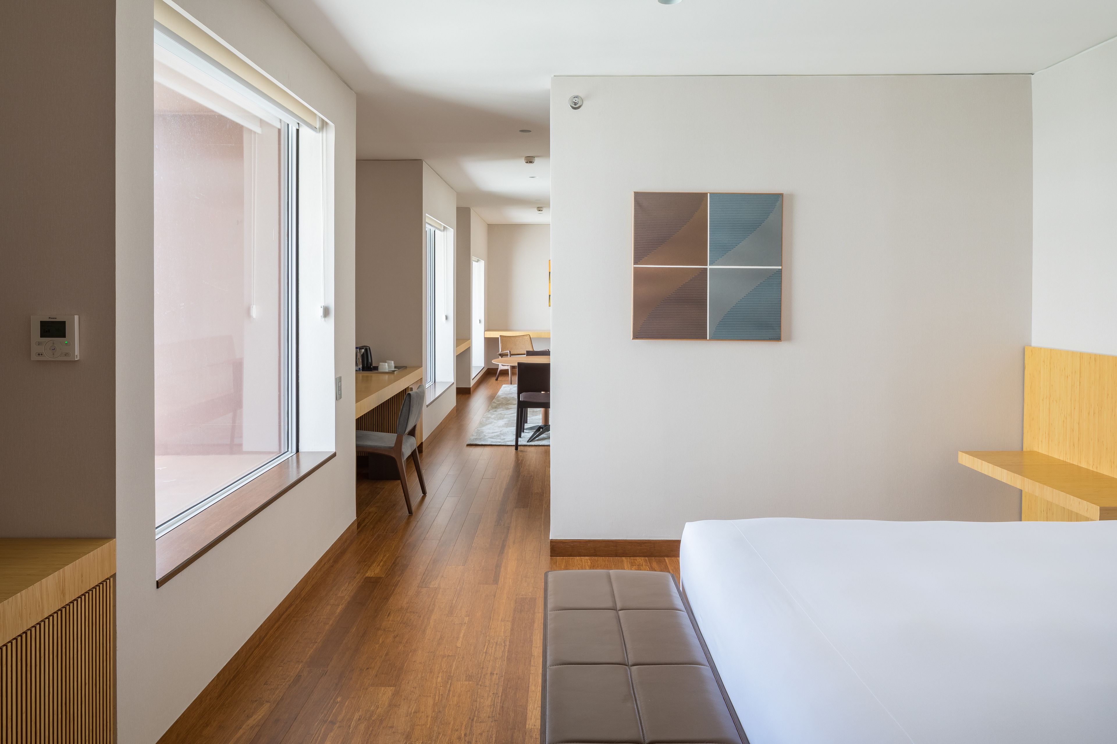 Une chambre d’hôtel moderne dotée d’une grande fenêtre, d’un banc en bois, d’un lit et d’un bureau avec une chaise.
