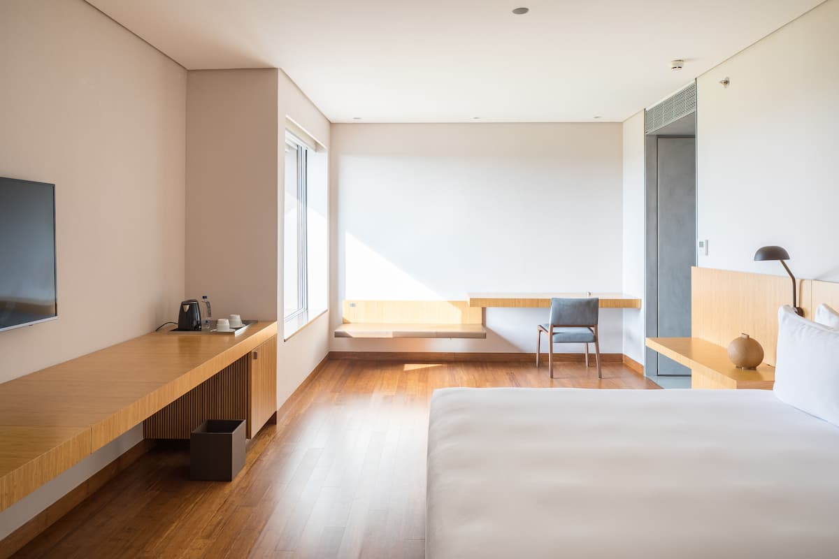 Een moderne hotelkamer met een houten bureau, een bed, een stoel en een groot raam.
