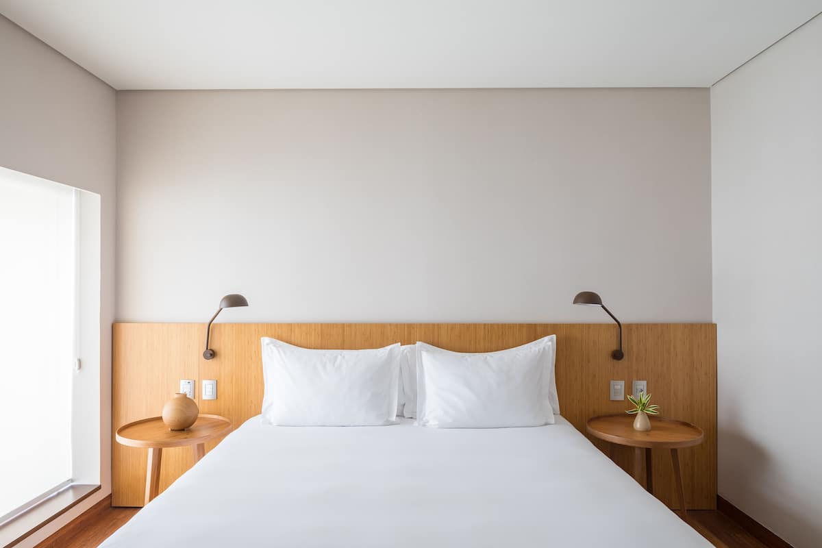 Een moderne hotelkamer met een groot bed, een houten hoofdeinde, twee nachtkastjes en een kleine plant in pot.