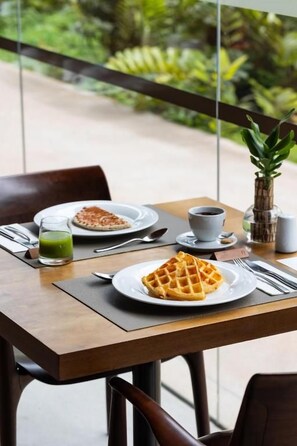 Ein Tisch mit einem Waffel, einer Kaffeetasse und einem grünen Getränk, vor einer grünen Kulisse.
