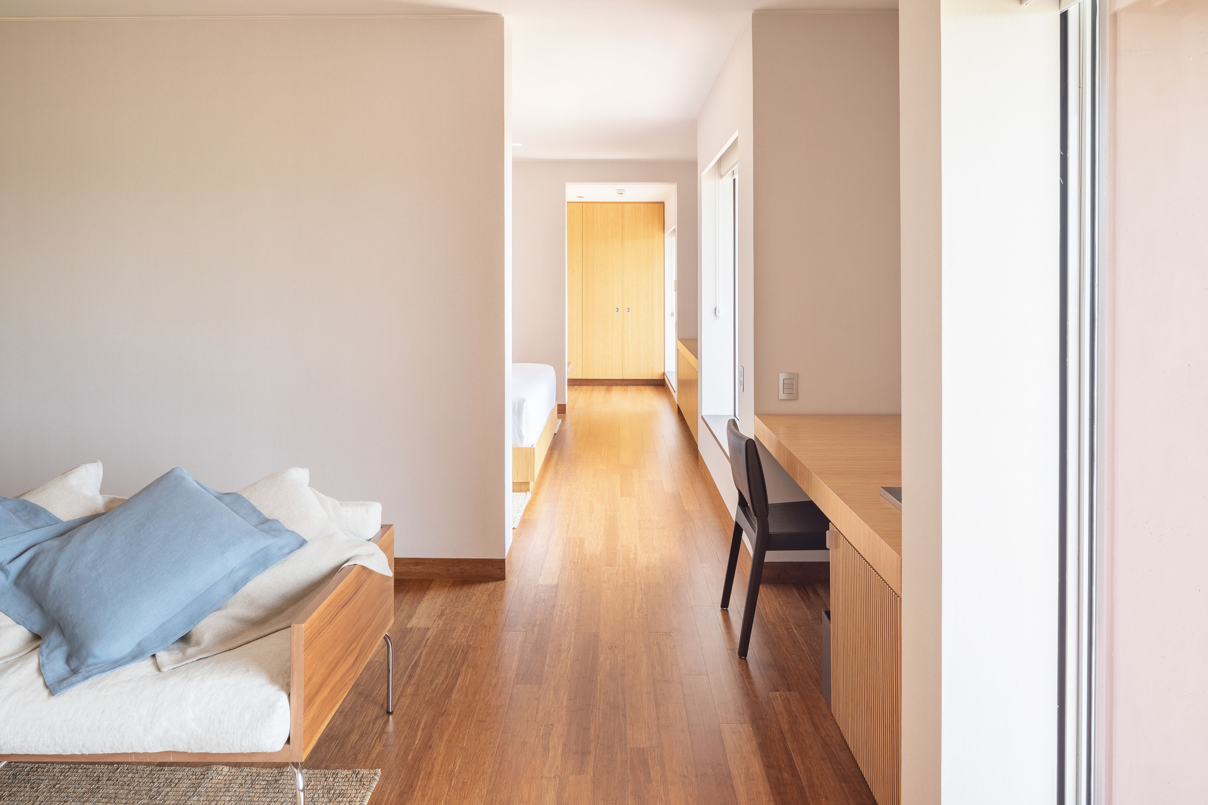A bedroom with a bed, a desk, and a wooden floor.