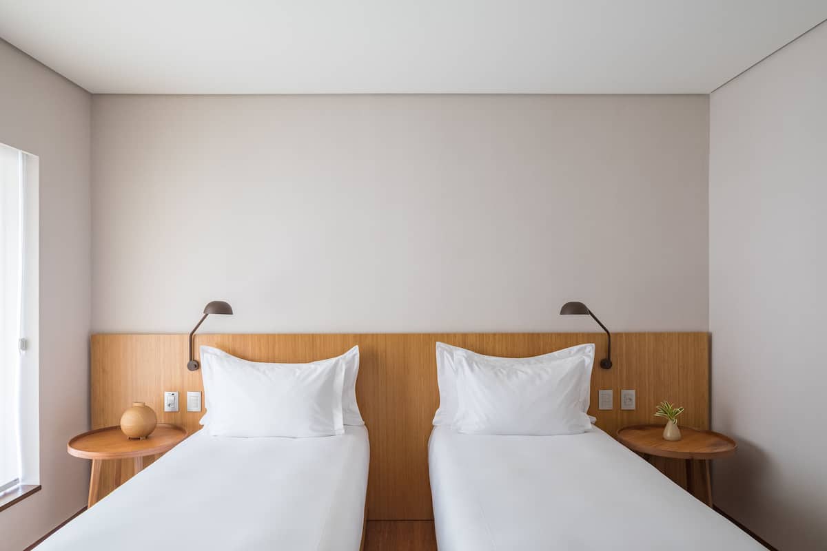 Een hotelkamer met twee bedden, houten hoofdborden, nachtkastjes met lampen en een kleine plant op een van de tafels.