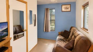 Une pièce avec un mur bleu, une porte en bois, un ventilateur de plafond, une fenêtre avec des rideaux, un canapé et un téléviseur posé sur un meuble en bois.