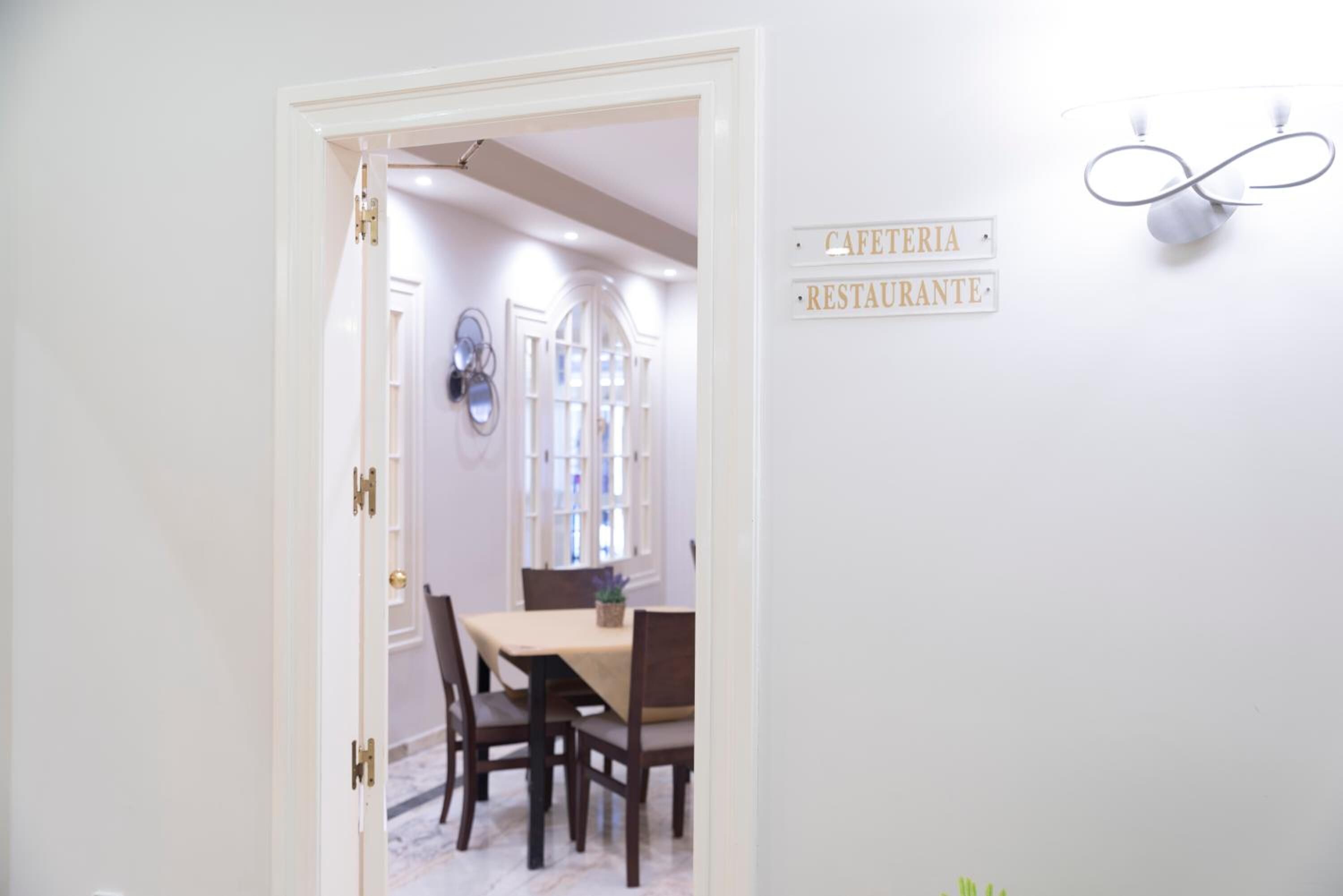 Un comedor con mesa y sillas, un letrero que indica cafetería y restaurante, y una lámpara de pared decorativa.