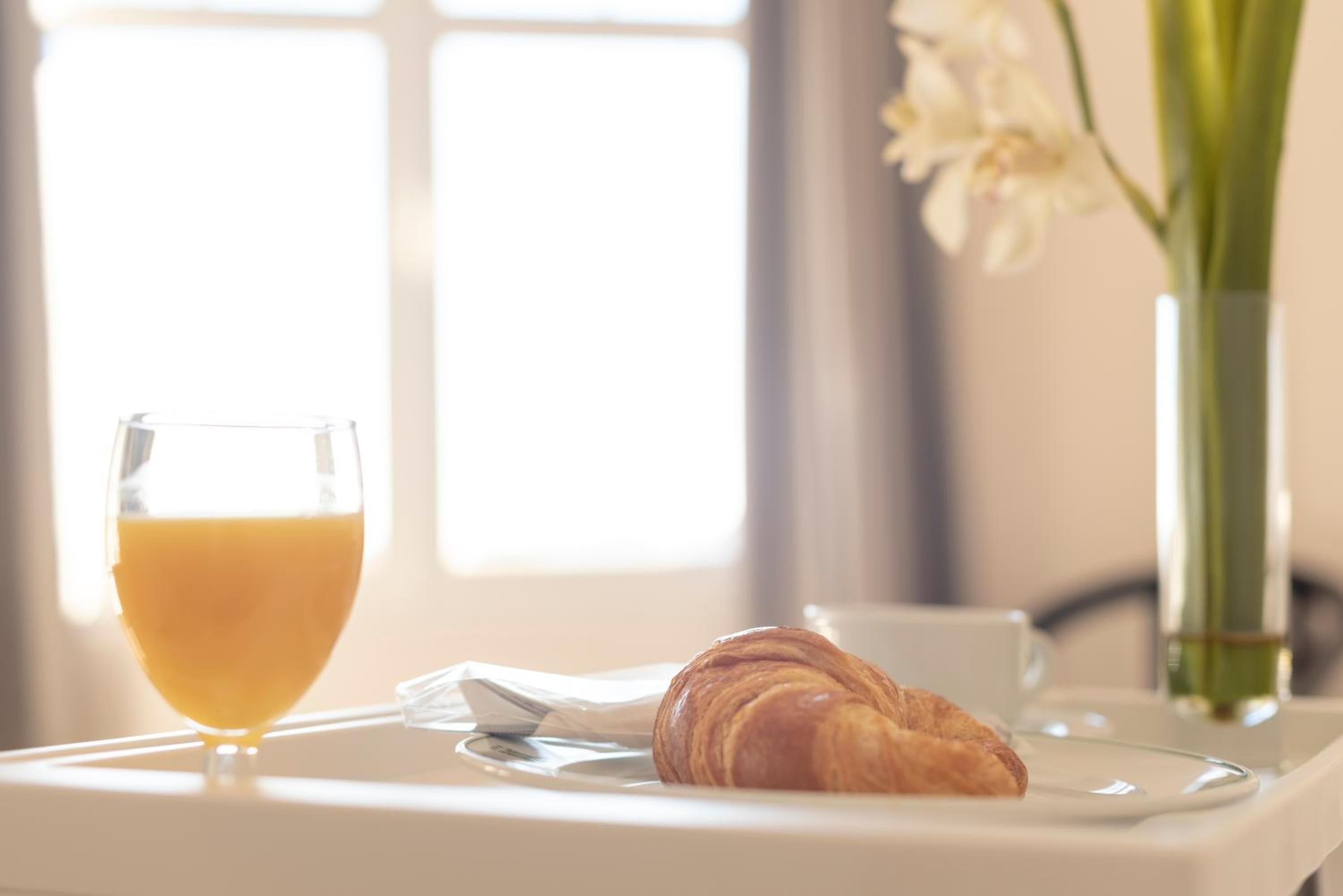Bandeja de desayuno con un croissant y un vaso de jugo de naranja sobre una mesa blanca.