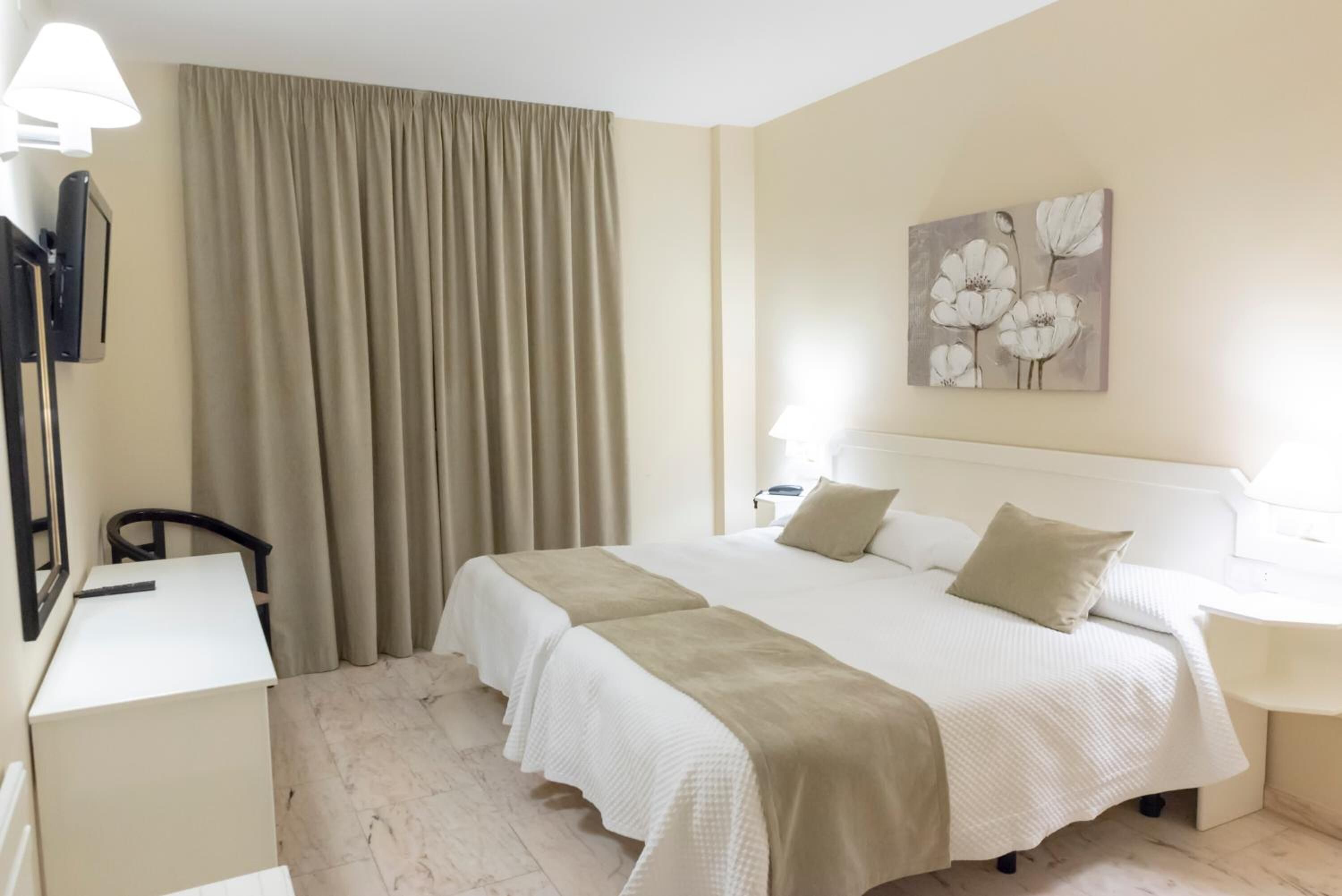 Habitación de hotel con una cama, un escritorio, una silla, una lámpara y un cuadro en la pared.