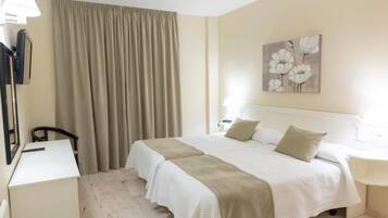 Habitación de hotel con una cama, un escritorio, una silla, una lámpara y un cuadro en la pared.