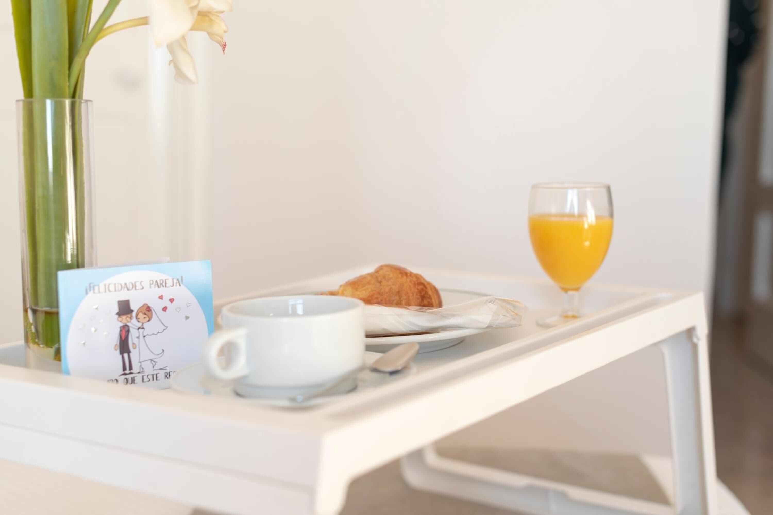 A breakfast tray with a croissant, a glass of orange juice, a cup, and a card on a white table.