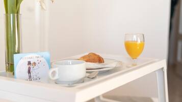 A breakfast tray with a croissant, a glass of orange juice, a cup, and a card on a white table.