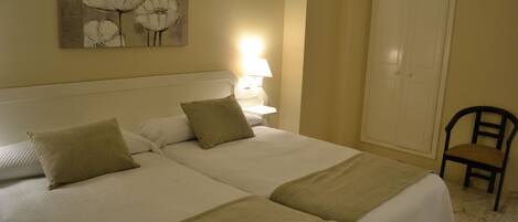 A double bed with two pillows and a blanket, a bedside table with a lamp, a chair, and a door.