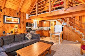 Interior acogedor de una cabaña con sala de estar, cocina y una escalera.