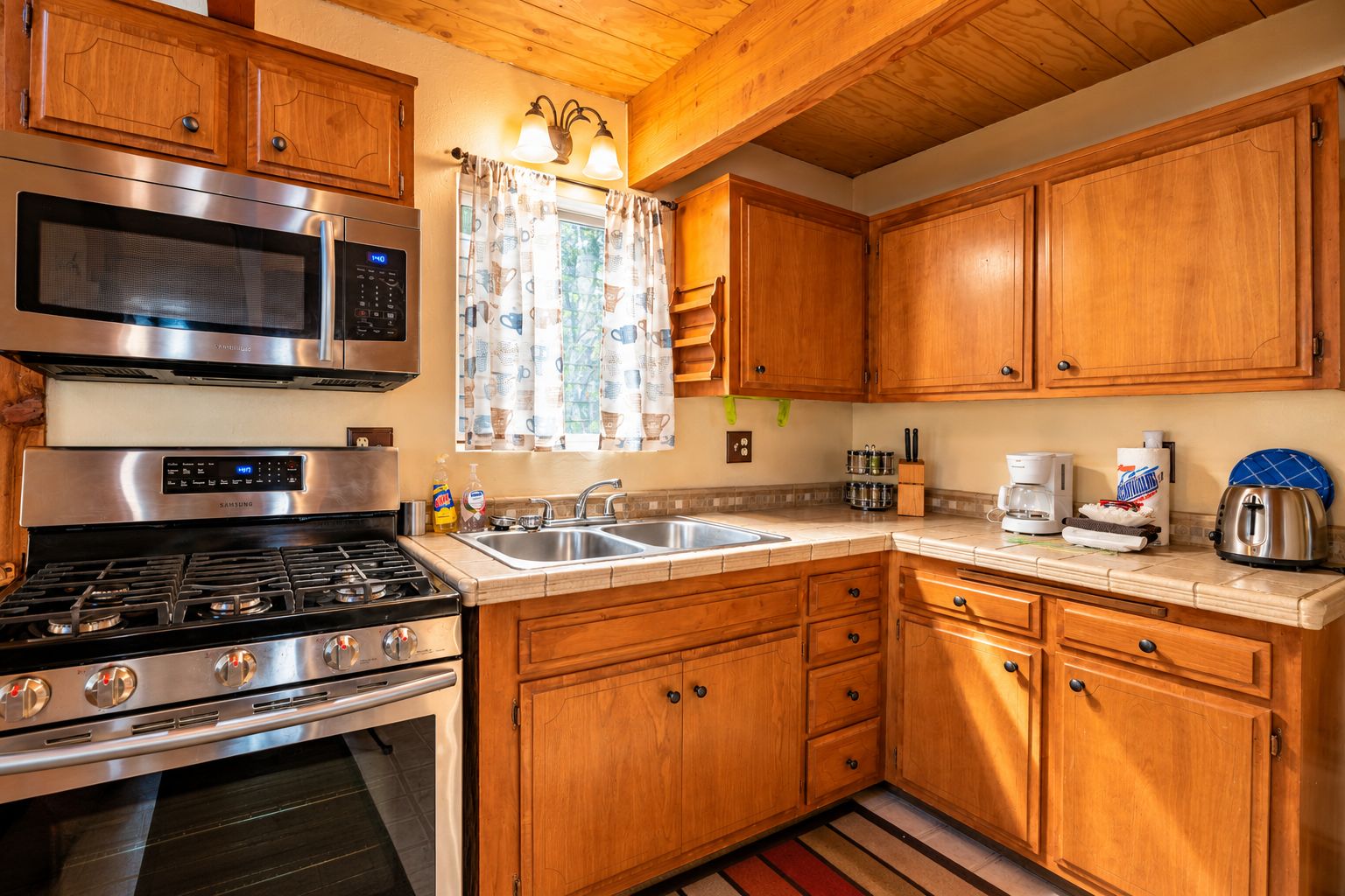 A kitchen with wooden cabinets, stainless steel appliances, and a window with patterned curtains.