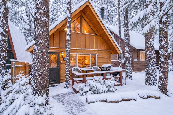 Una cabaña de madera con un porche cubierto, rodeada de árboles cubiertos de nieve.