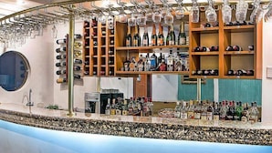 Una zona de bar con estantes llenos de botellas y vasos, una barra con diferentes botellas, y un espejo redondo en la pared.