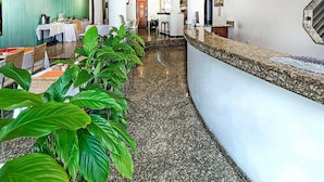 Un vestíbulo de hotel con una recepción, una pared verde y una larga fila de mesas y sillas.