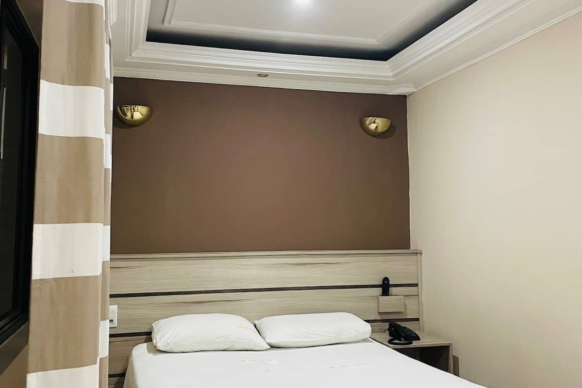 Ett hotellrum med en säng, ett sängbord och en telefon som är monterad på väggen.
