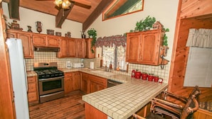 Una cocina con armarios de madera, salpicadero de azulejos, una isla central y un comedor con una silla.