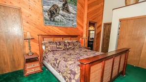 Un dormitorio con paneles de madera, una cama, una mesita de noche, una lámpara y un cuadro con osos en la pared.