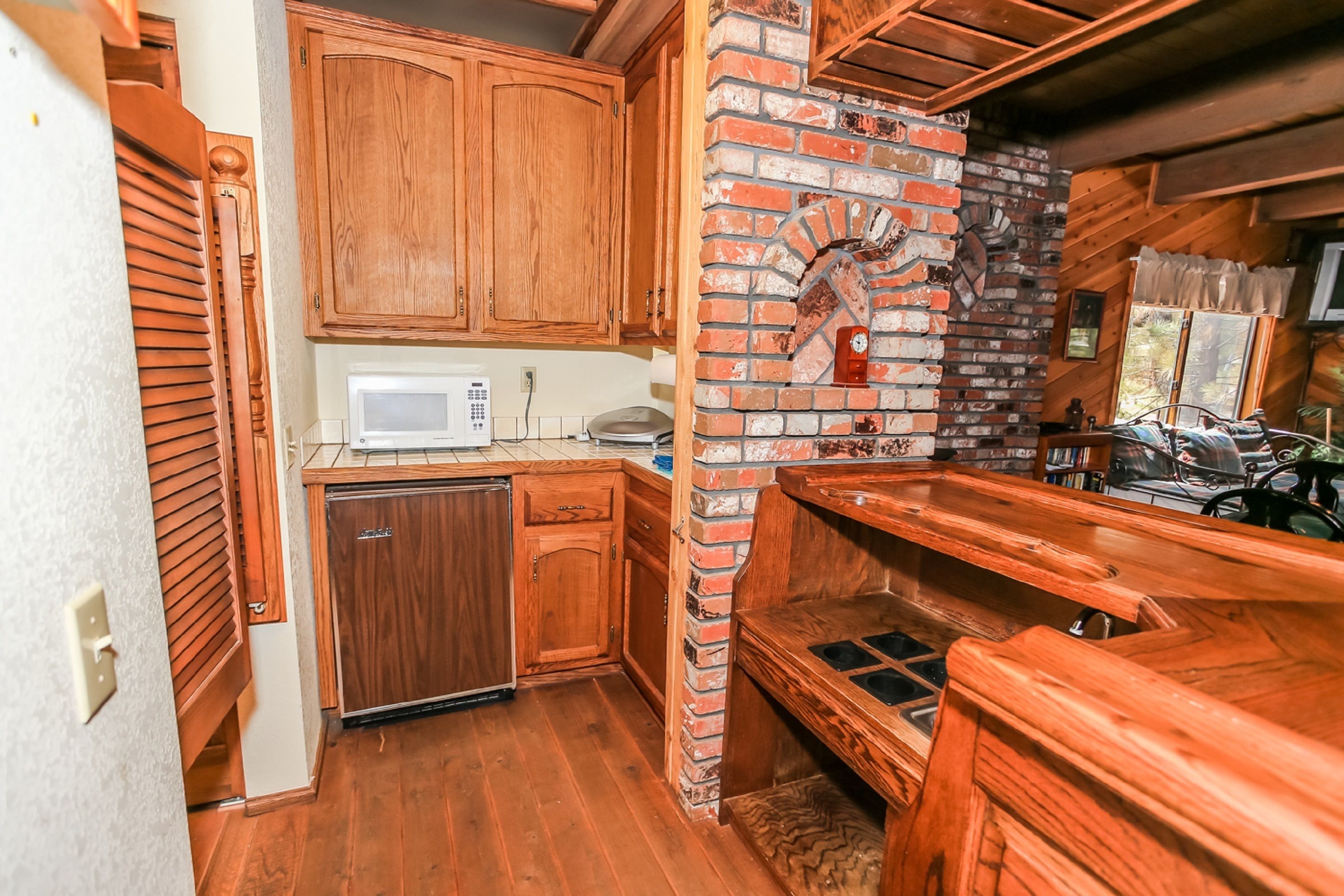 A compact kitchen with wooden cabinets, a brick oven, and a microwave.