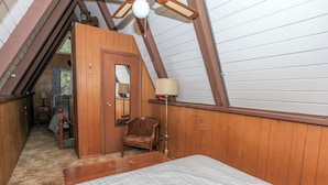 A bedroom with a sloped ceiling, wooden walls, a bed, a chair, and a lamp. - The Getaway (Big Bear Lake)