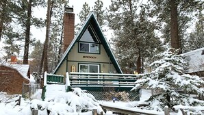 A cabin with a triangular roof, a wooden deck, and a sign that reads "Our Get Away". - The Getaway (Big Bear Lake)