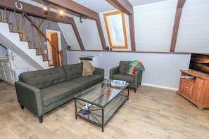 Un salón estilo loft con una mesa de centro de vidrio, dos sofás, un aparador de madera y una escalera con vigas a la vista.