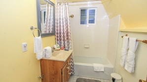 A bathroom with a wooden vanity, a sink, a mirror, a shower curtain, a window, and a toilet. - The Getaway (Big Bear Lake)