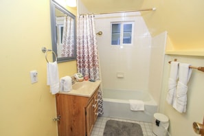 A bathroom with a wooden vanity, a sink, a mirror, a shower curtain, a window, and a toilet.
