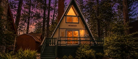 A cabin with a steeply pitched roof, a front porch, and a chimney.