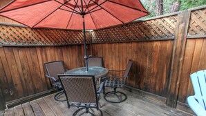 A wooden deck with a round table and four chairs, an umbrella, and a wooden fence. - The Getaway (Big Bear Lake)