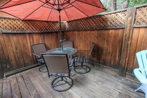 A wooden deck with a round table and four chairs, an umbrella, and a wooden fence.