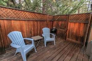 Un patio al aire libre con dos sillas Adirondack y una pequeña mesa, rodeado por una valla de madera y árboles al fondo.