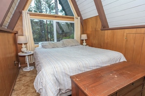 Un dormitorio con una cama grande, dos lámparas de noche, una mesita de noche de madera y una ventana con vistas a árboles.