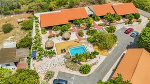 Vista aérea de un resort con piscina, palmeras y un edificio de techo rojo.