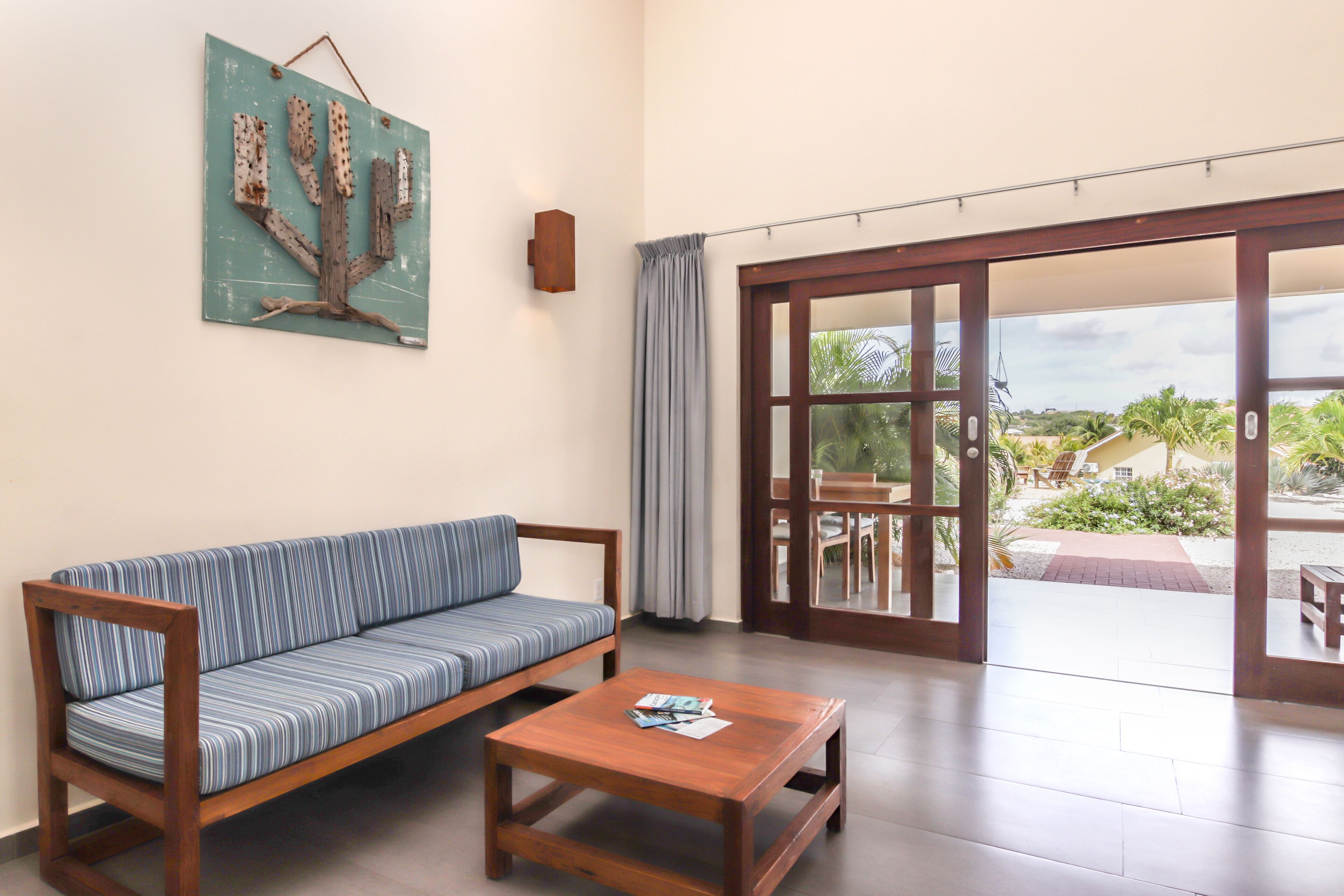 A room with a wooden sofa, a small wooden table, and a large sliding glass door leading to an outdoor area with a view of greenery.