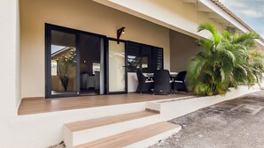Un área de estar exterior moderna con terraza de madera, puerta de vidrio y una planta en maceta.