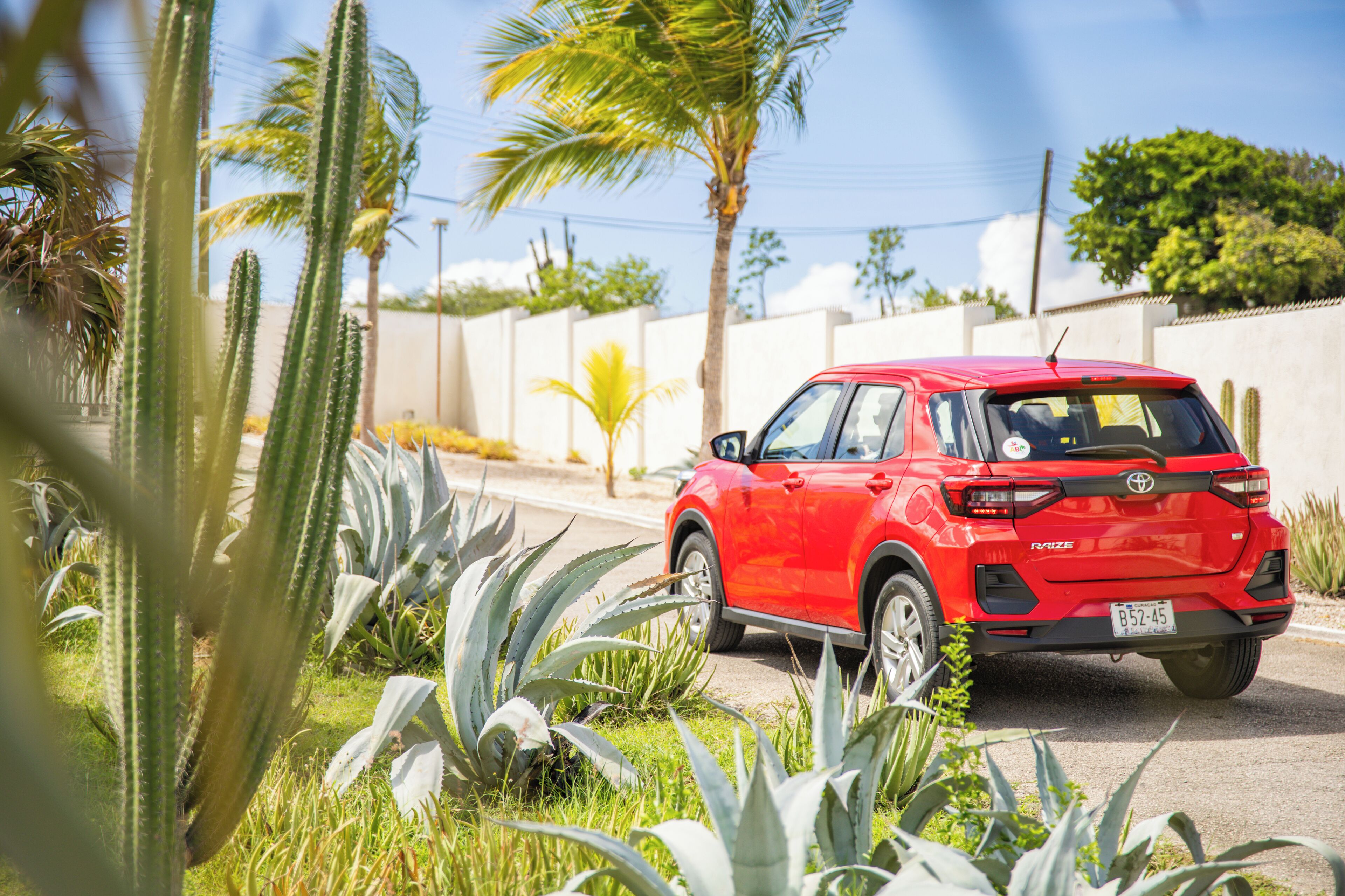 Punainen Toyota RAV4 -malli on pysäköity kadulle, taustalla näkyy kaktuksia ja palmuja.