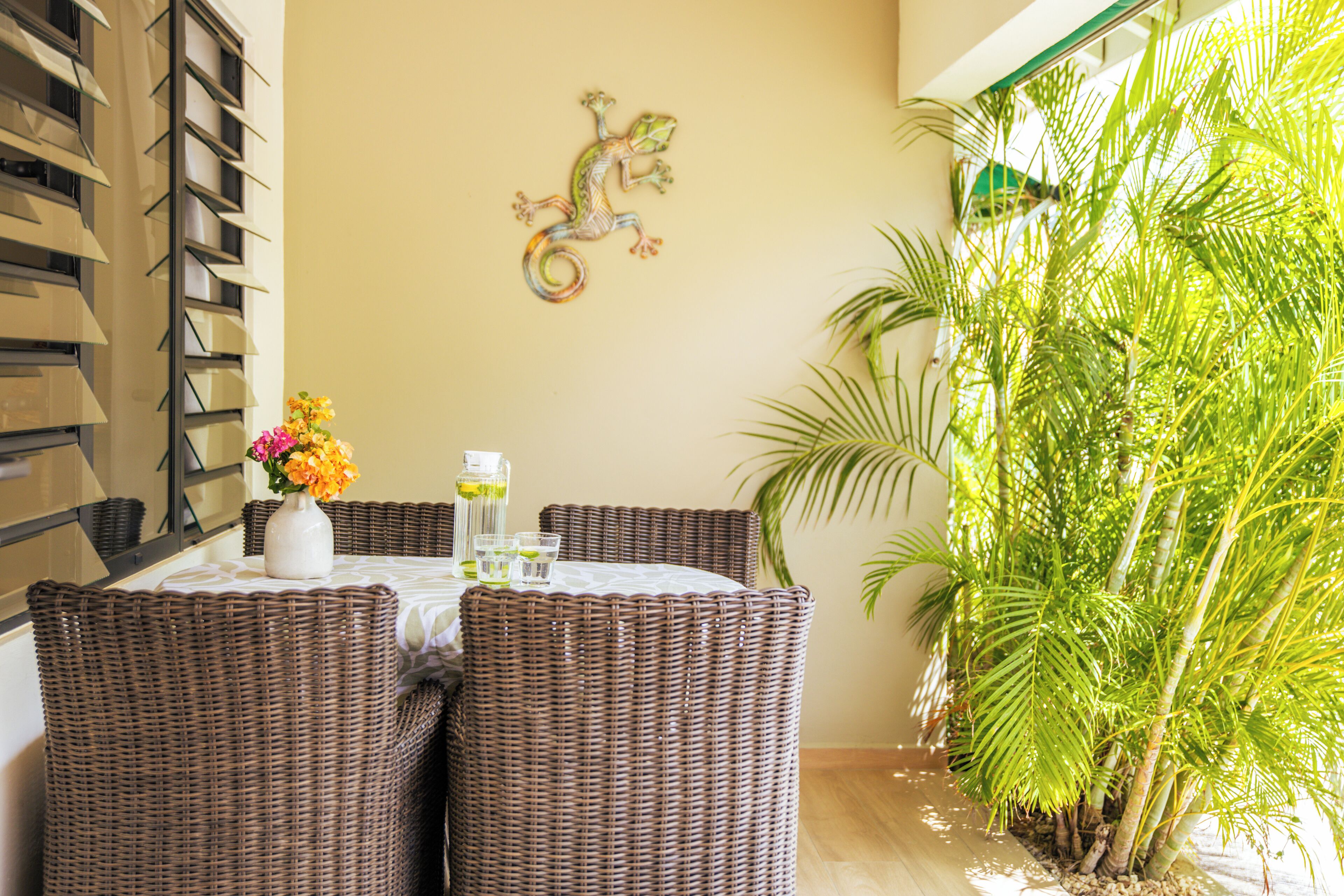 A dining area with wicker furniture, a table with a vase of flowers, and a wall-mounted lizard decoration.