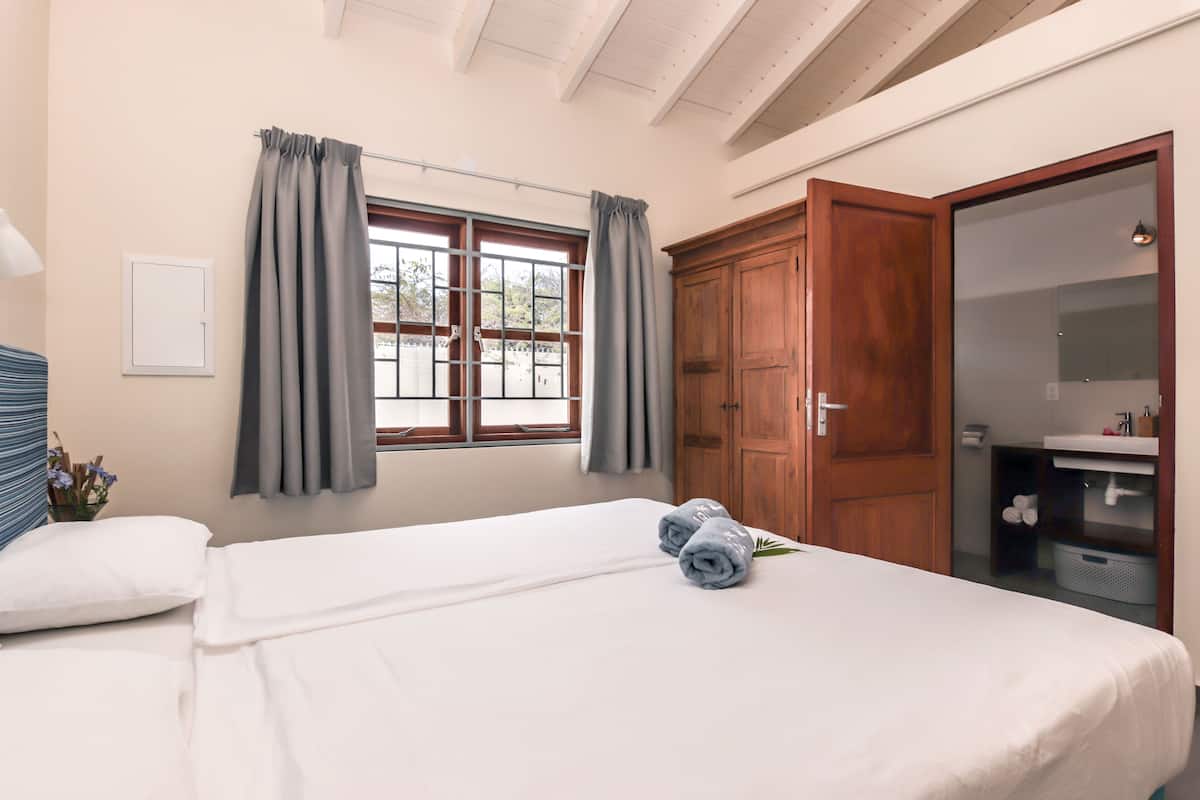 A hotel room with a bed, a window with curtains, a wooden wardrobe, and a bathroom with a mirror and sink.