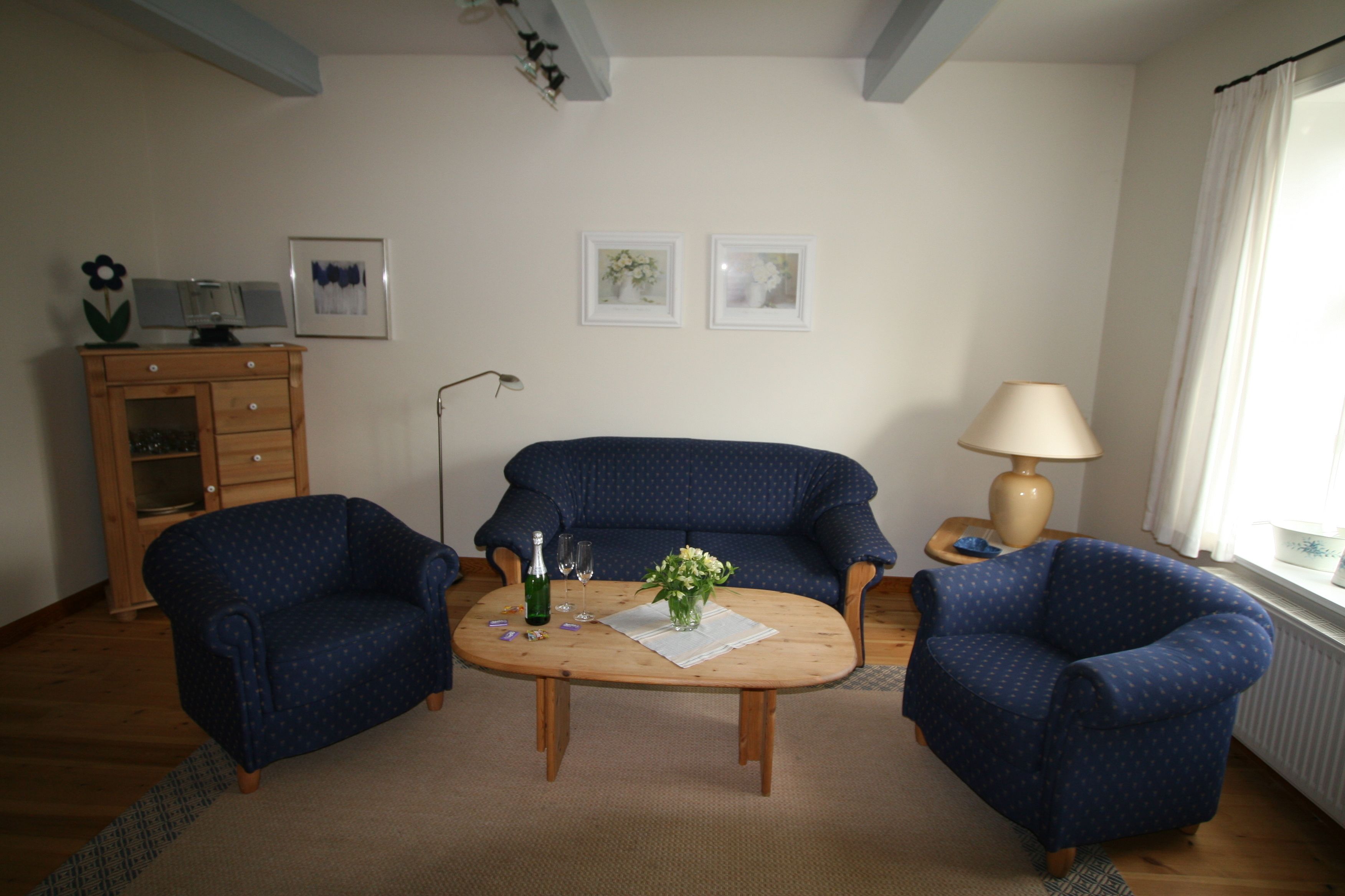 A living room with two blue armchairs, a wooden coffee table with a vase of flowers, a lamp, and a cabinet with a flower decoration.