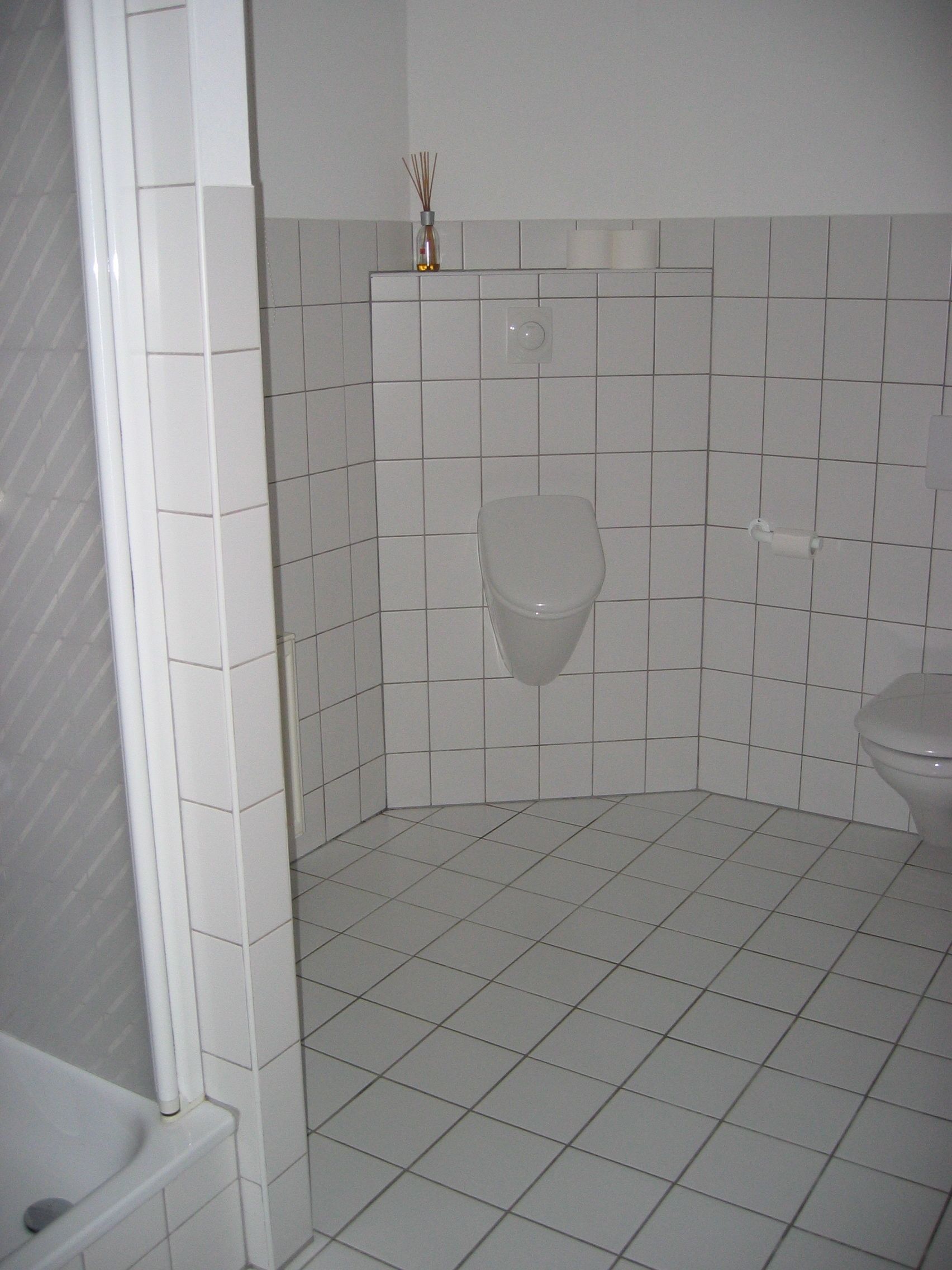 Un baño pequeño con azulejos, que incluye un inodoro, un orinal y una zona de ducha.