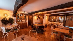 Un coin repas rustique avec des tables et des chaises en bois, un bar doté de meubles en bois et une grande fenêtre laissant entrer la lumière naturelle.