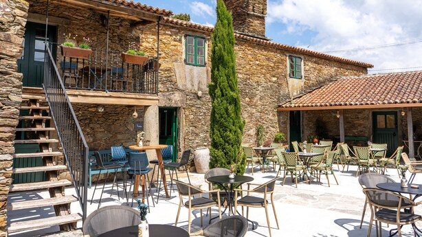 Un bâtiment en pierre doté d’une terrasse, d’un escalier et d’un grand arbre.
