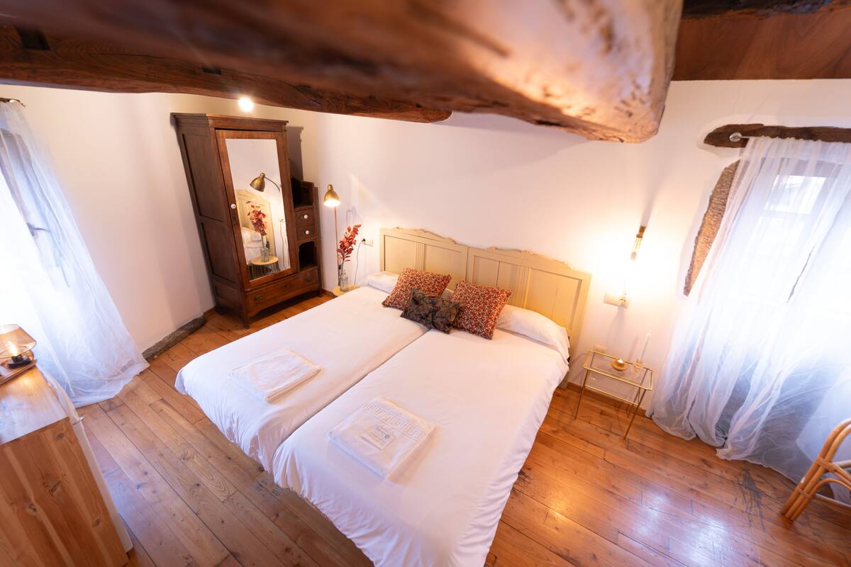 Ein Doppelbett mit weißer Bettwäsche, ein Holzkapfenster, ein Spiegel und ein Nachttisch mit Lampe.