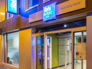 Exterior de un hotel ibis budget con entrada de vidrio, señalización que dice 'Paris Chilly Mairie' y un coche visible al fondo.