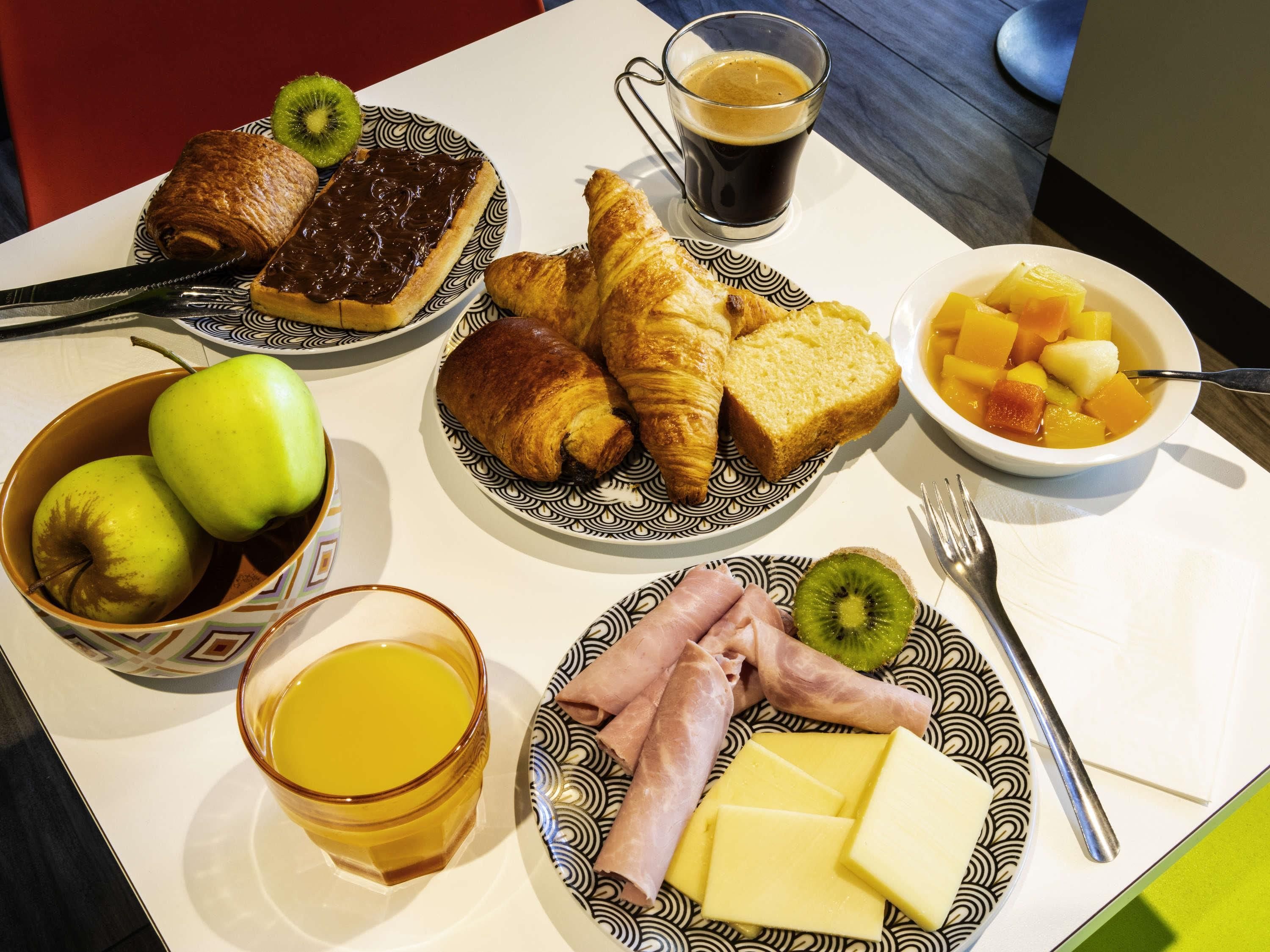 A breakfast setting with croissants, apples, cheese, ham, and a bowl of fruit.