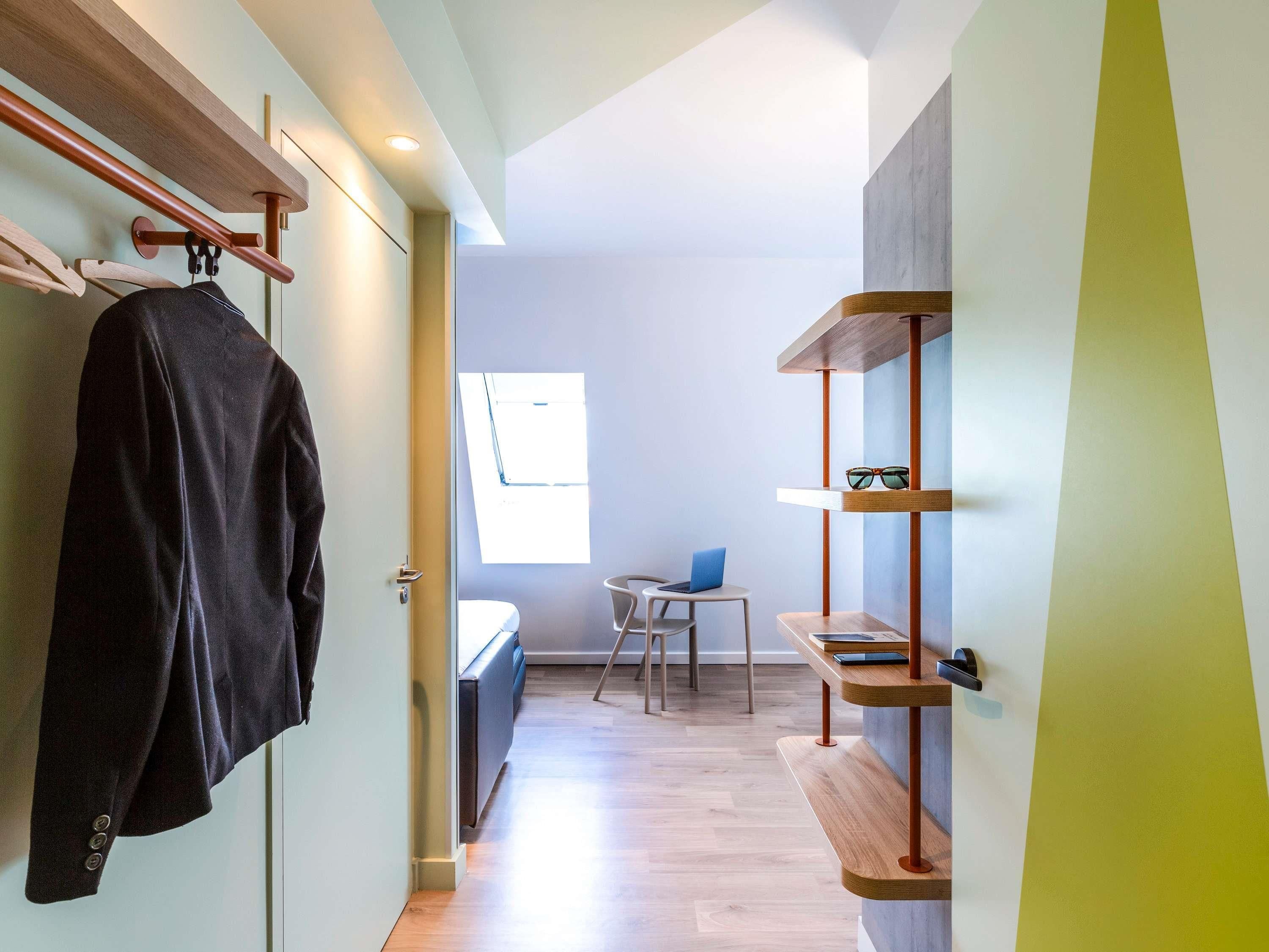 Un intérieur moderne avec un banc en bois, un porte-manteau et une petite table sur laquelle se trouve un ordinateur portable.